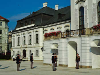 People walking by buildings in city against sky