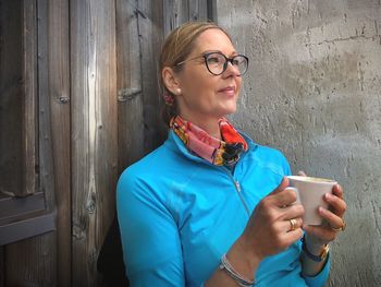 Smiling woman holding coffee cup against door