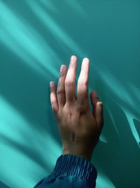 Close-up of human hand by wall during sunny day