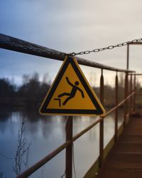 Close-up of warning sign on bridge over lake against sky