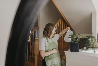 Woman standing by potted plant at home