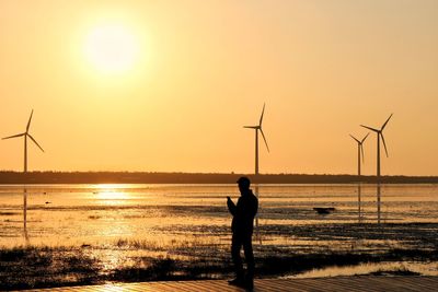 Silhouette man fishing in sea against sunset sky