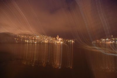 Illuminated city by river against sky at night