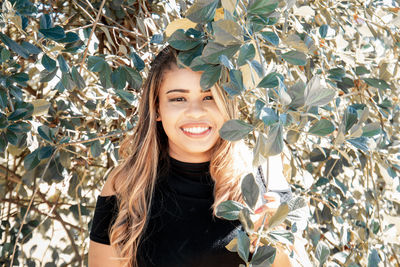 Portrait of smiling young woman standing below tree