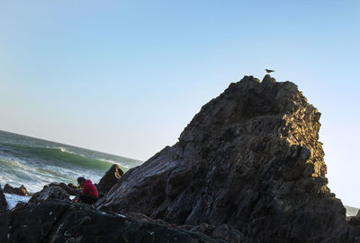 People on rock by sea against clear sky