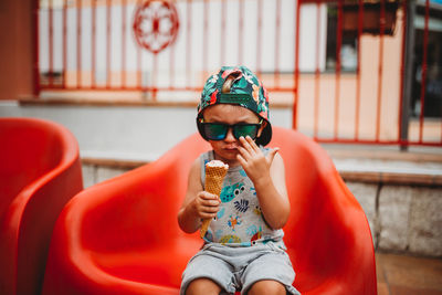 White male toddler eating ice cream with sunglasses and cap to back