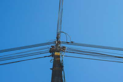 Low angle view of electricity pylon against clear blue sky