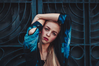 Portrait of beautiful young woman standing against metal gate