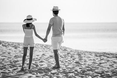 Rear view of men on beach against sky