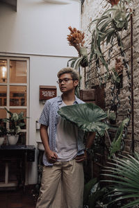 Portrait of young man standing against potted plants