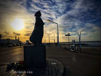 Man on footpath by sea against sky during sunset