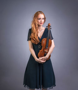 Portrait of beautiful woman holding violin against gray background