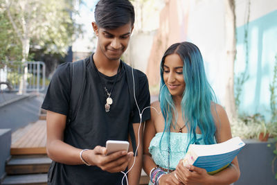 Happy friends using mobile phone outdoors