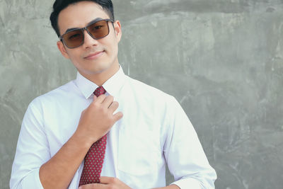 Portrait of smiling man wearing sunglasses standing against wall