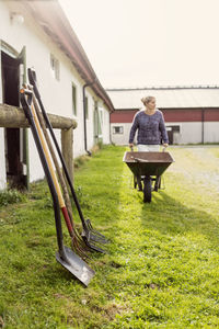 Female farmer walking with wheelbarrow by equipment at farm