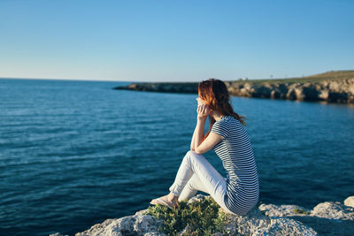 Woman sitting on rock looking at sea against sky