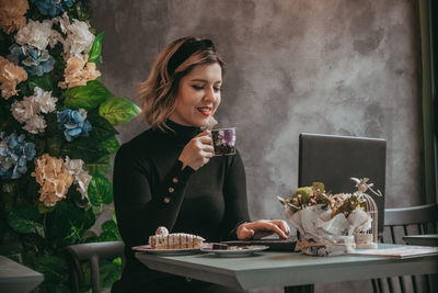 Young woman drinking from glass while sitting on table