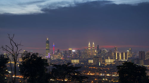 Illuminated buildings in city against cloudy sky