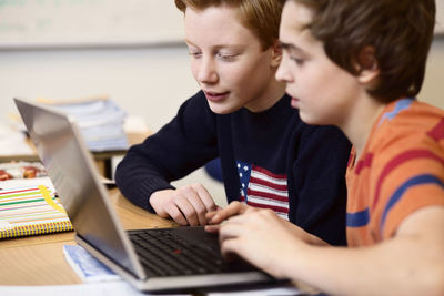 High school boys using laptop at desk in classroom