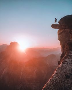 Low angle view of man standing on cliff against sky during sunset