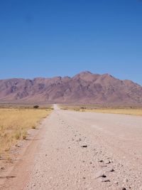 Road leading towards mountains against clear blue sky