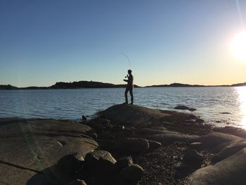 Man standing on rock at beach against clear sky