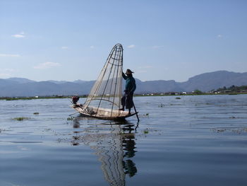 Man fishing in lake against sky