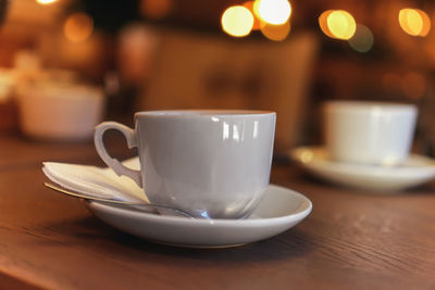 White tea cup standing on saucer in soft focus on naturally blurred background with bokeh lights