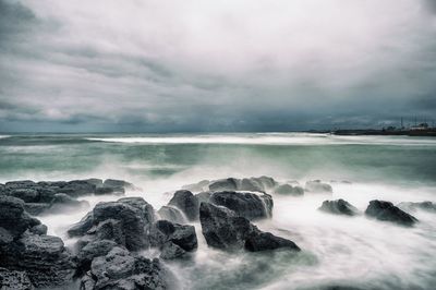 Rocks at beach against cloudy sky