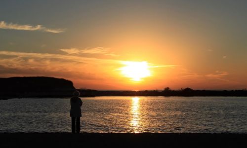 Silhouette man standing on beach against orange sky