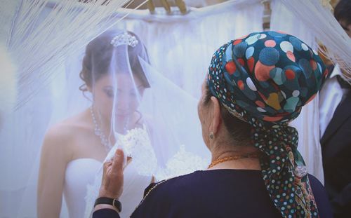 Woman adjusting veil of bride during wedding ceremony