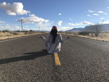 Rear view of woman on road against sky in peaceful pose