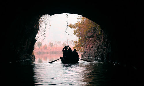 Silhouette people sitting in cave against sky