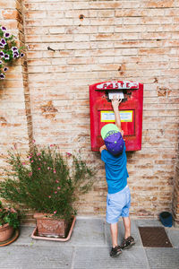 Rear view of boy putting letter in mailbox