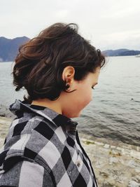 Side view of girl standing on steps by lake against cloudy sky