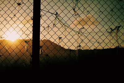 Silhouette chainlink fence against sky during sunset