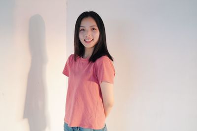 Portrait of smiling young woman standing against wall