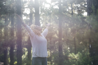 Low angle view of woman with arms outstretched standing in forest