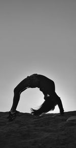 Silhouette man climbing on sand against clear sky