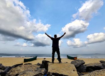 Rear view of man standing on rock at beach against sky