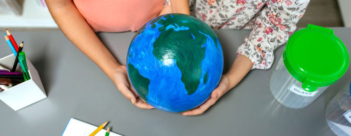 Two unrecognizable female students holding handmade globe world earth