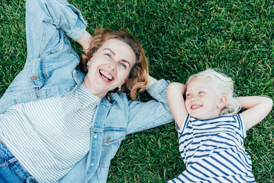 Top view of carefree cheerful mother and daughter lying on green grass and enjoying summer