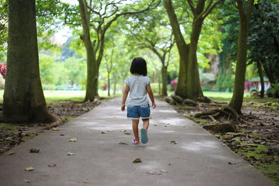 Rear view of a child walking on footpath amidst trees during day in asia