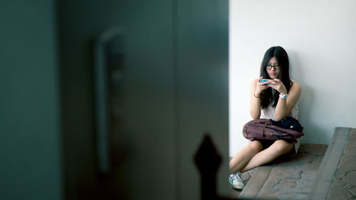 Young woman using mobile phone while sitting on wall