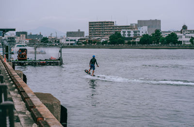 Man on sea by city against sky