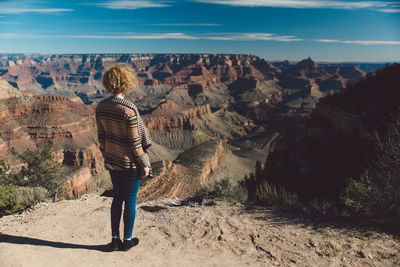 Rear view of woman standing on rock formation against sky