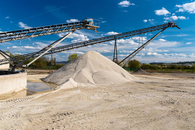 Conveyor over heaps of gravel on blue sky at an industrial cement plant.