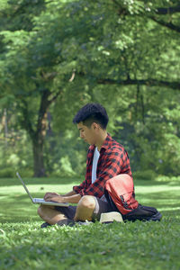 Young man using mobile phone while sitting on tree