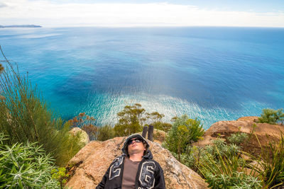High angle view of young man lying on rock by sea against sky