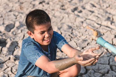 Close-up of smiling boy with hands cupped sitting by faucet